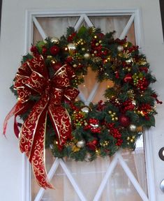 a christmas wreath on the front door of a house with red and gold ornaments around it