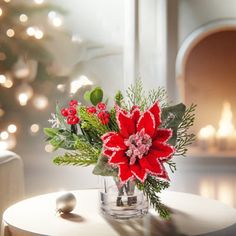 a glass vase filled with red flowers sitting on top of a table next to a christmas tree