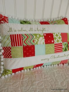 a decorative pillow is sitting on a white bed with red, green and blue pillows