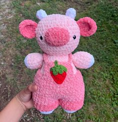 a small pink stuffed animal with a strawberry on it's chest is held up in the air