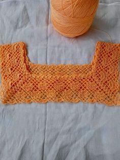 an orange crocheted piece of cloth next to a ball of yarn