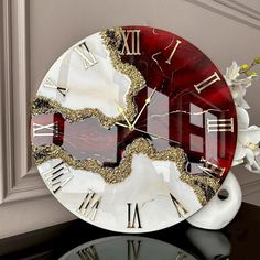 a red and white clock sitting on top of a table next to a vase with flowers