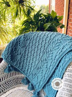 a blue knitted blanket sitting on top of a white chair next to a potted plant