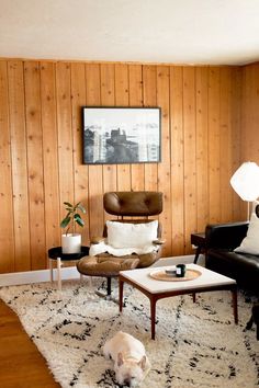 a living room with wood paneling and black leather chairs, white rugs, and a dog laying on the floor