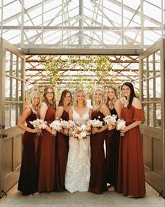 a group of women standing next to each other in front of a wooden structure holding bouquets