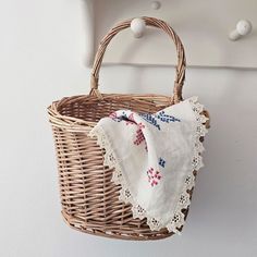 a wicker basket hanging on the wall with a white cloth in it and an embroidered handkerchief