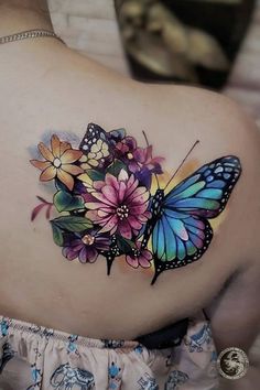 a woman with a butterfly tattoo on her back shoulder and flower bouquets around it