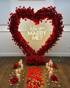 a heart - shaped arrangement with candles and roses on the floor in front of a sign that says will you marry me?