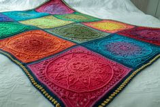 a multicolored crocheted blanket on a bed with white sheets and pillows