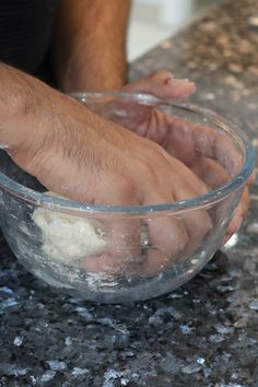 a person mixing something in a bowl on top of a granite counter with their hands