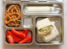 a lunch box with a sandwich, pretzels, and peppers on the side