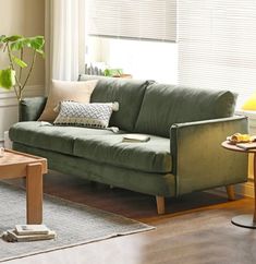 a living room with a green couch and coffee table in front of the window,