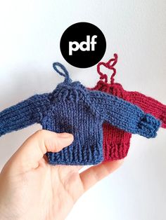 a hand is holding two knitted sweaters