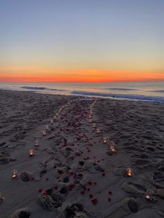 candles are lined up in the sand on the beach as the sun sets over the ocean