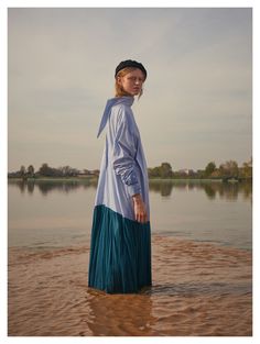 a woman is standing in the water wearing a blue and white dress with pleated skirt