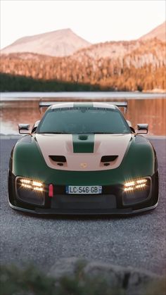 a green and white sports car parked in front of a lake