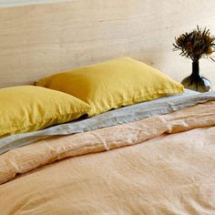 two yellow pillows on top of a bed next to a vase with flowers in it