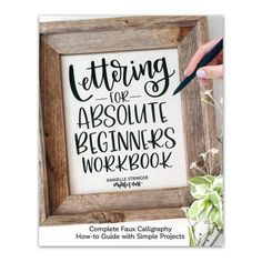 a hand holding a pen over a wooden frame with the words lettering for absolute beginners workbook