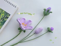 three crocheted flowers sitting on top of a table next to an open book