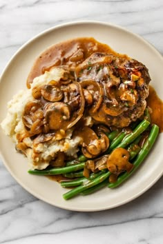 a white plate topped with mashed potatoes and green beans covered in mushroom gravy