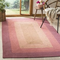 a pink and beige area rug in front of a window with a wicker chair next to it