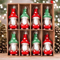 twelve christmas ornaments in a box on a table with pine cones and lights behind them