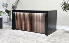 a black cabinet with wooden slats on the front and sides next to potted plants