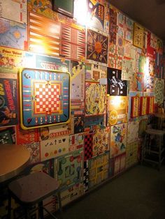 a wall covered in lots of colorful pictures and lights next to tables with stools