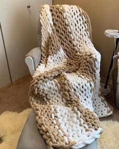 a white and brown blanket sitting on top of a gray chair next to a wall