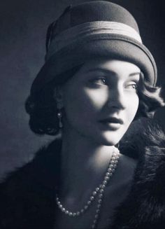 black and white photograph of a woman wearing a hat with pearls on her necklaces