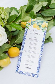 a menu card sitting on top of a table next to lemons and flowers with greenery around it