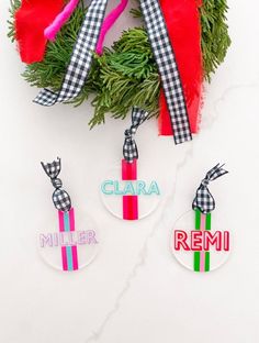 christmas wreath with ribbon and name tags hanging from it's side on a white surface