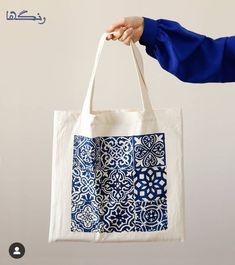 a person holding a white bag with blue and white designs on it, in front of a gray background