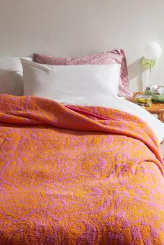 an orange and pink bedspread on a white bed