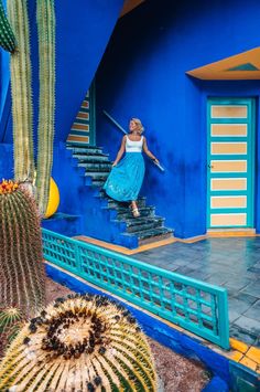 a woman in a blue dress is walking up the stairs to a house with cactus and cacti