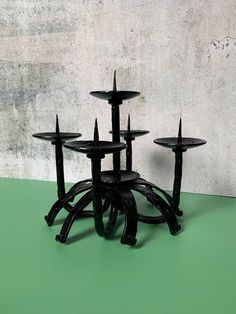 four black candlesticks are arranged on a green surface