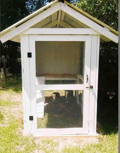 a small white chicken coop in the grass