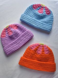 three crocheted hats are laying on a white tablecloth, one is blue and the other is orange