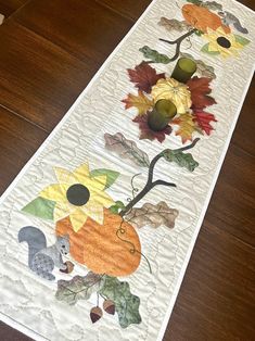 a quilted table runner with autumn leaves and flowers on the border, along with an acorn