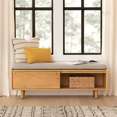 a wooden bench sitting in front of a window with pillows on it and a book