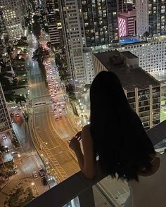 a woman standing on top of a tall building looking at the city lights in the distance