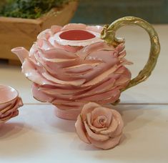 a tea pot and two cups are sitting on a table with pink flowers in it