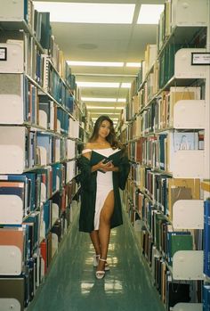 a woman is walking down the aisle in a library with lots of books on shelves