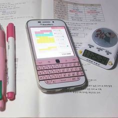 a pink cell phone sitting on top of an open book next to a pen and calculator