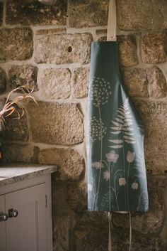 a teal bag hanging on a stone wall next to a white cabinet and vase