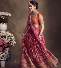 a woman in an orange and pink lehenga standing next to a vase with flowers