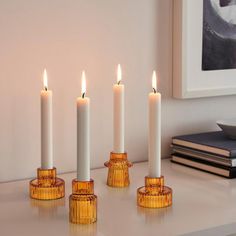 four candles sitting on top of a white table next to a book and some books