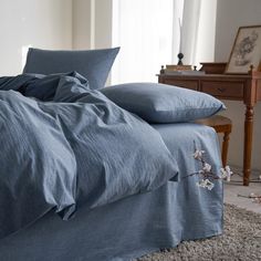 an unmade bed with blue linens in a bedroom next to a dresser and window