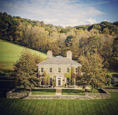 a large house in the middle of a lush green field with trees and bushes surrounding it