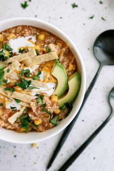 a white bowl filled with chili, cheese and avocado on top of a table